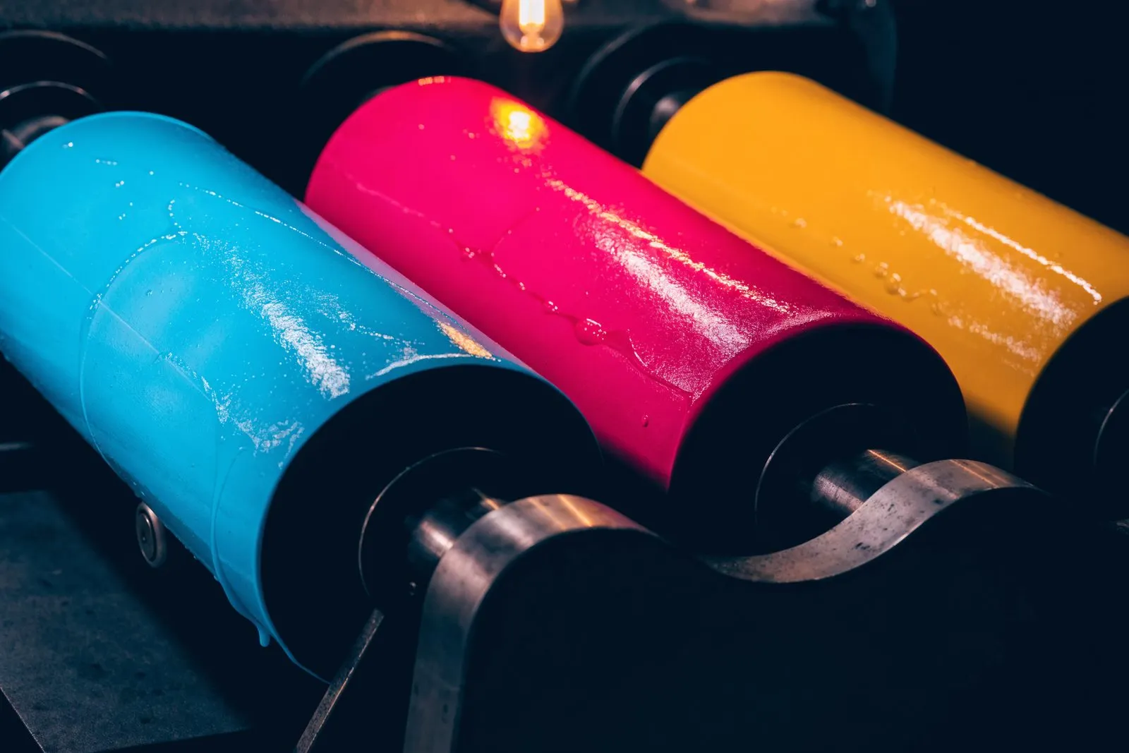 Farbwalzen einer Offsetmaschine, glänzend benetzt mit Cyan, Magenta und Gelb