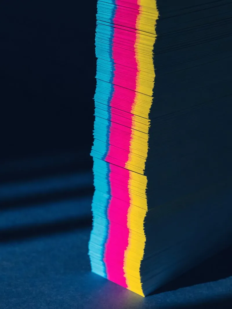 Hoher Stapel frisch geschnittener Bogen, an der Kante ein Farbband in Cyan, Magenta und Gelb