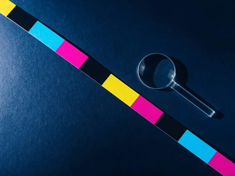 Farbkontrollstreifen in Cyan, Magenta, Gelb und Schwarz mit einer kleinen Lupe