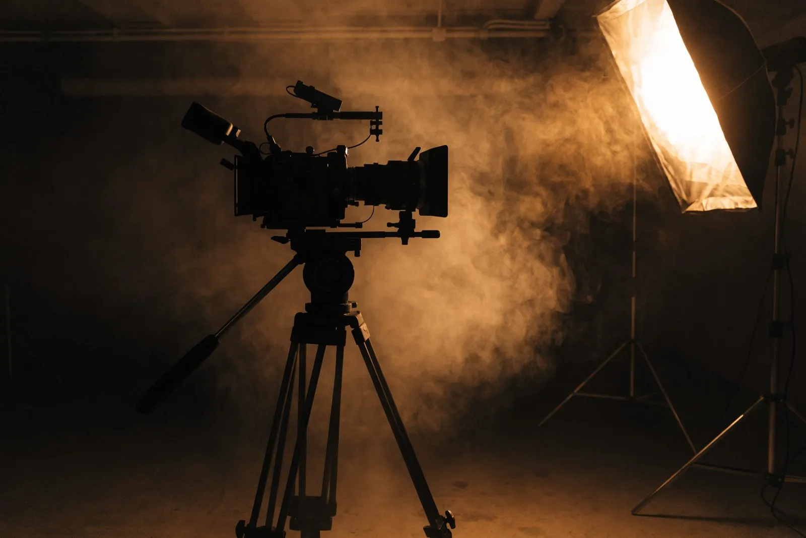 Filmkamera auf Stativ als Silhouette vor einem dunklen Studio, warm angeleuchtet