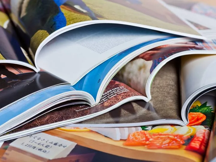 Mehrere aufgeschlagene Magazine mit farbigen Bildseiten, übereinandergelegt