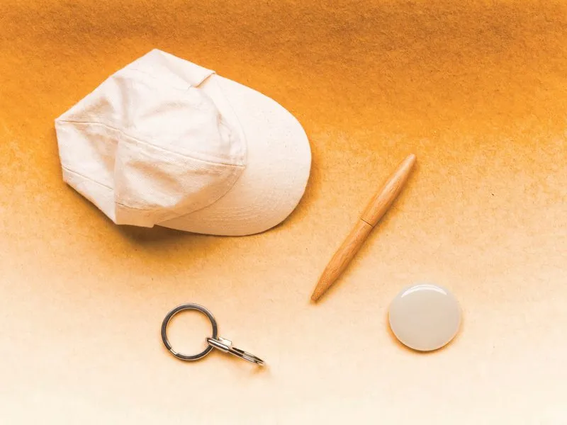 Kleine unbedruckte Werbeartikel von oben: Kappe, Stift, Schlüsselring und Button