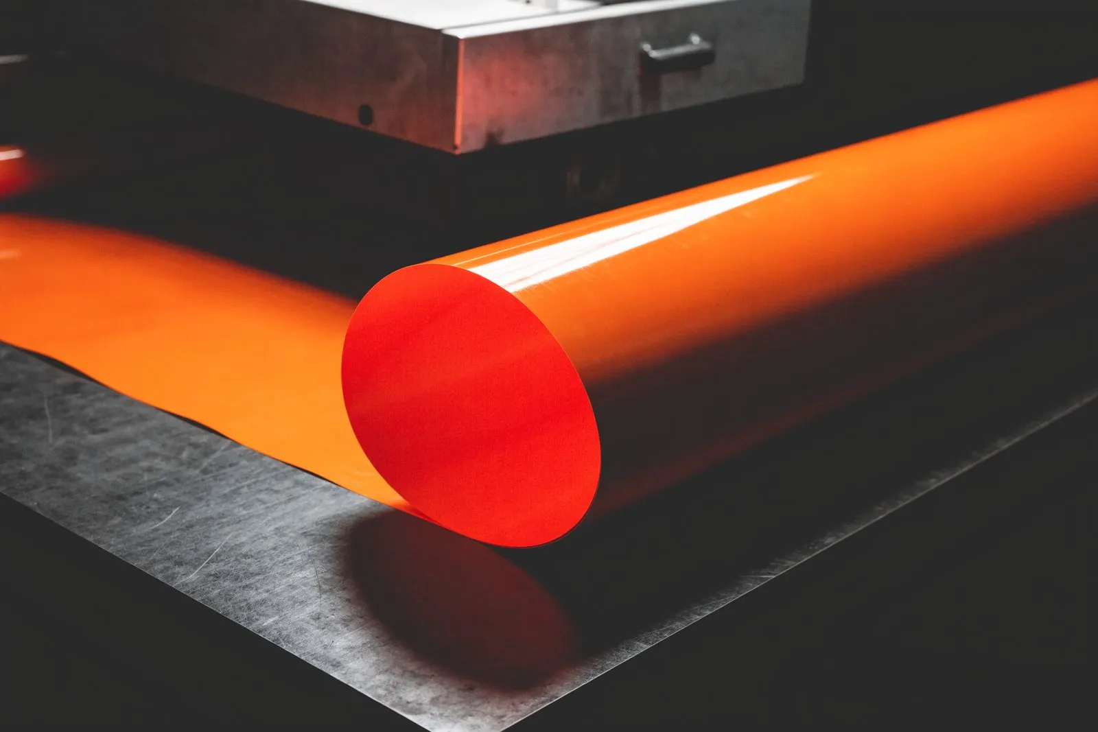 Breite Rolle signalorange Folie, teilweise über eine dunkle Werkbank abgerollt