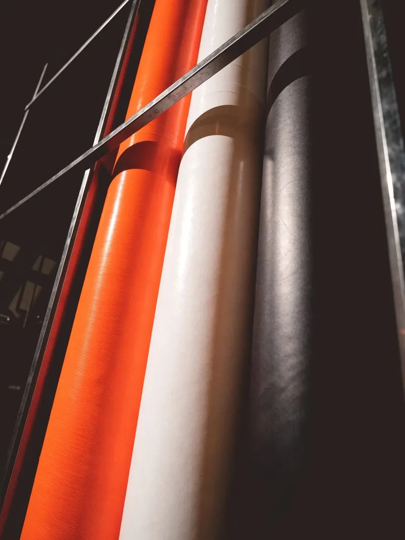 Folienrollen in Orange, Weiß und Anthrazit stehen aufrecht nebeneinander im Regal