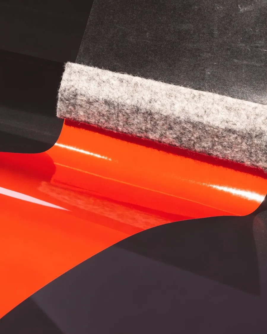 Rakel drückt eine orange Folienbahn auf eine glatte dunkle Fläche